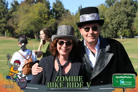 A couple in elegant black Victorian costumes and top hats smile together.