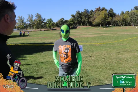 A boy in a green alien costume stands alone in an open field.