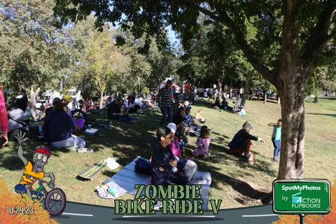 Festival-goers relax on blankets in the shade of large trees.