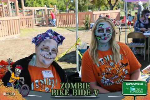 Two women show off skull face paint in matching orange shirts.