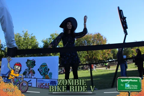 A woman in a witch costume waves with both arms raised at the finish line.