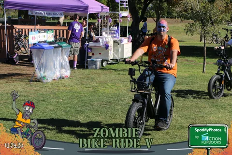 A man rides an orange e-bike past festival vendor tents.
