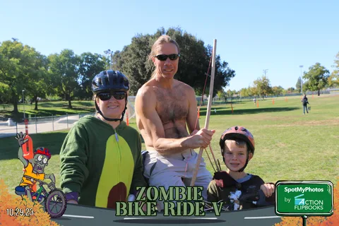 A man in a green cape costume poses playfully with a child.