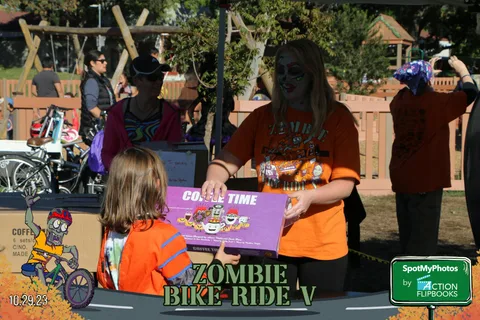 A volunteer hands a costume contest prize box to a girl in a witch hat.