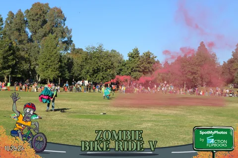 A skydiver stands on the grass with pink smoke trailing as a crowd watches from a distance.