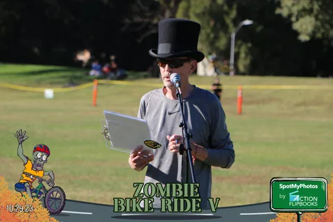 A man in a top hat speaks into a microphone while reading from a paper.