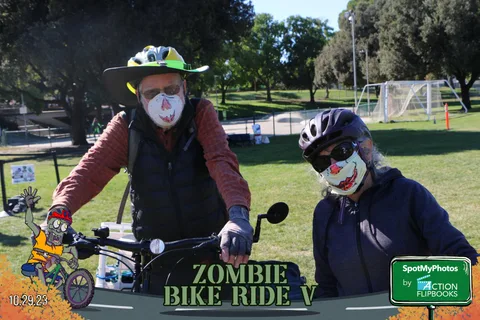 A masked rider in costume sits on a bike with another rider nearby.