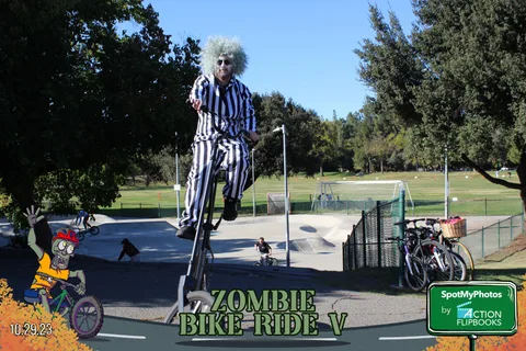 A rider dressed as Beetlejuice balances high on a tall bike at the skate park.