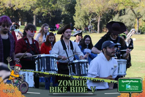 A drumline performs along a taped-off barrier with a volunteer nearby.