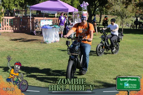 Two cyclists ride past a purple event tent in the park.