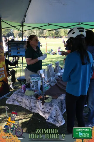 A volunteer under a canopy hands an item to a young girl at an information booth.