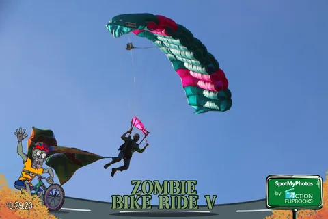 A skydiver flips upside down mid-air beneath a striped parachute canopy.