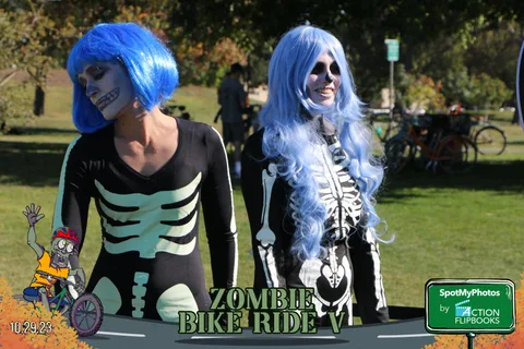 Two women in elaborate skeleton makeup and a blue wig pose together.