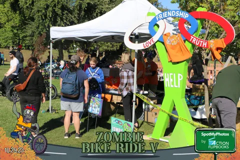 A person in a green costume stands near festival booths under colorful ring decorations.