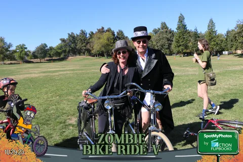A couple in Victorian costume poses together on a bicycle.