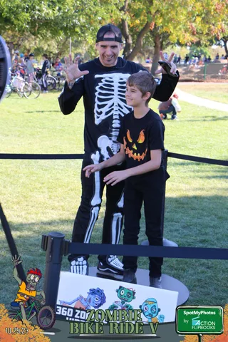 A man and boy in skeleton costumes pose and wave for the camera.