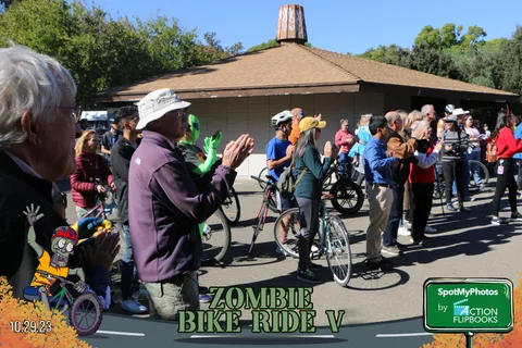 An older man claps along with the crowd as cyclists gather behind him.