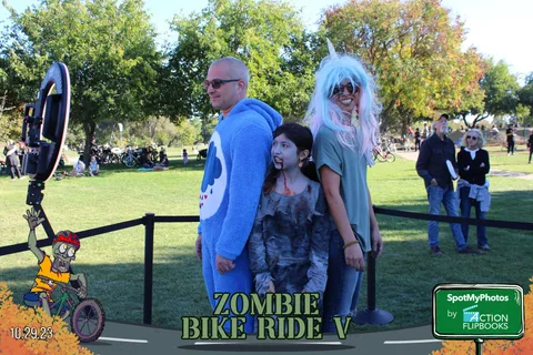 A family poses in a blue onesie, zombie face paint and a unicorn wig at the finish line.