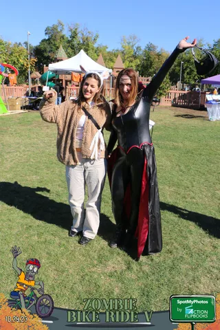 Two costumed women raise their arms joyfully with festival tents behind them.