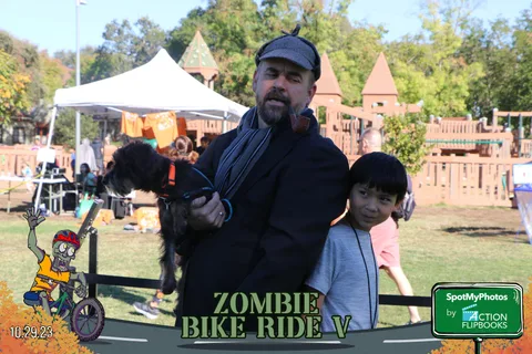 A man stands with a dog and a child near Halloween-themed tent decor.