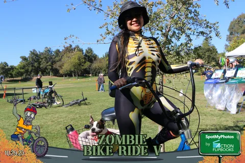 A woman in a striped costume poses with her bike and a dog in the basket.