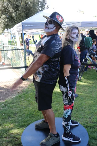 A man and woman in matching skull face paint pose together under a festival tent.