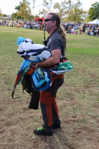 A skydiver carries his gathered parachute across the park after landing.