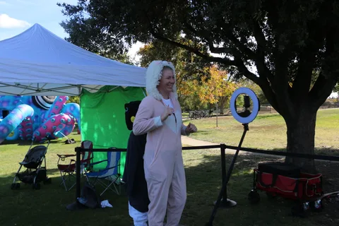 A person in a fluffy costume stands sideways at the green screen photo booth.