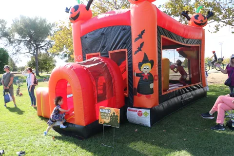 A red Halloween-themed inflatable bounce house sits in the park.