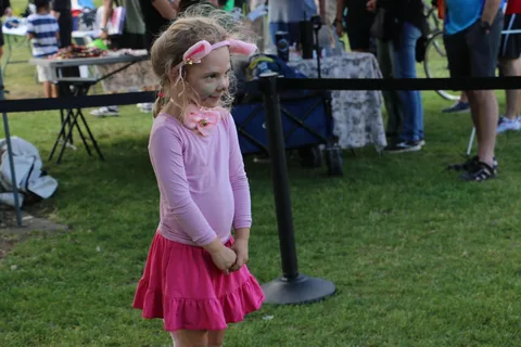 A young girl in a pink skirt and ear headband poses quietly on the grass.