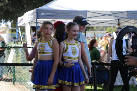 Two young cheerleaders in matching gold and blue uniforms smile together at the festival.