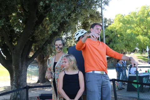 A costumed family stands together as the father points toward something offscreen.