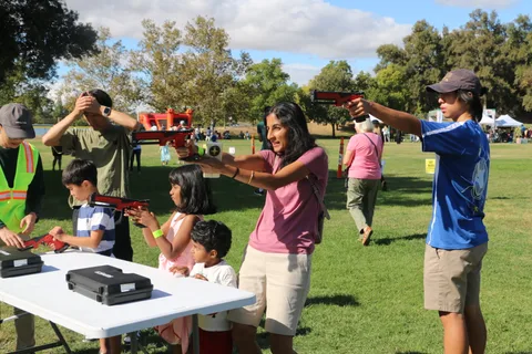 A family aims toy blasters together at an activity booth.