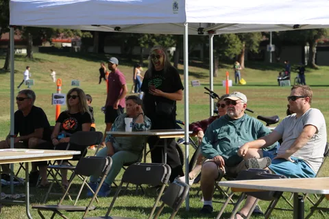 A group of people sit together at tables under a canopy tent.
