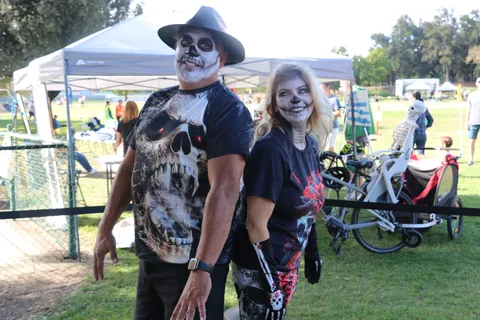 A man tips his cowboy hat beside a woman in skull makeup, bikes parked behind them.