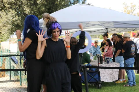 Two women in blue wigs wave cheerfully at the camera.