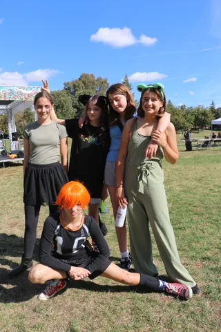 Three girls in ear headbands pose together smiling in the park.