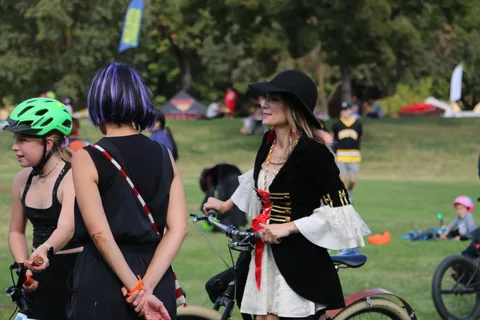 Two women in costume ride bikes away from the camera.