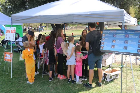 Kids and parents gather under a tent at a festival information booth.
