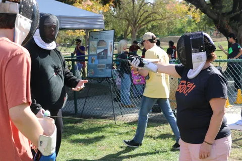 Two people in fencing masks practice with foils at an activity booth.