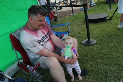 A father holds his baby while seated near the green screen photo booth.