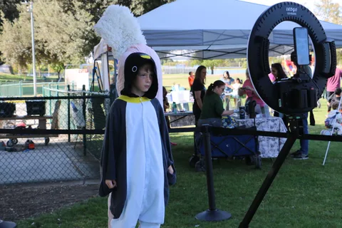 A child in a penguin costume stands under an event tent.