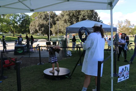 A person balances on a spinning platform as a photographer records at the booth.