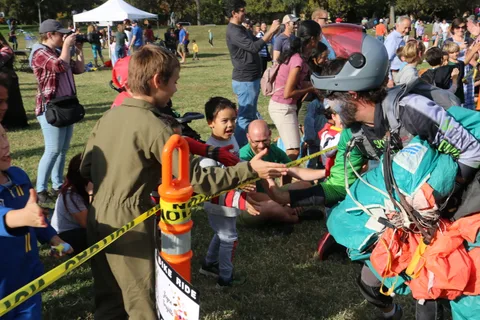 A man in an army costume shakes hands with a zombie-painted skydiver near a traffic cone.