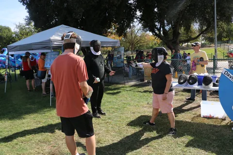 Two people stand with their backs to the camera near a park activity booth.