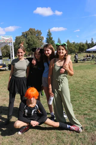 Three girls with animal ear headbands stand together in the park.