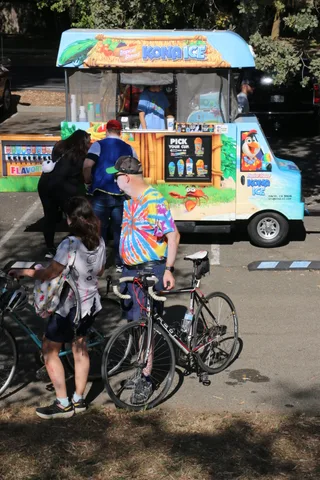 A cyclist in a colorful costume waits near an ice cream truck.