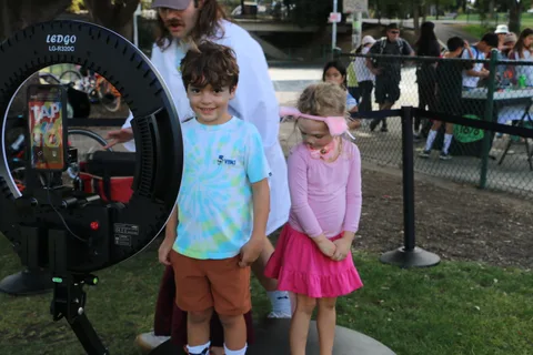 A family stands together near photo booth equipment with a crowd in the background.