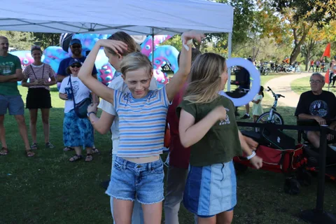 Two girls dance together near a balloon display at the festival.
