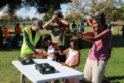 A group holds toy blasters up during an activity at a park booth.